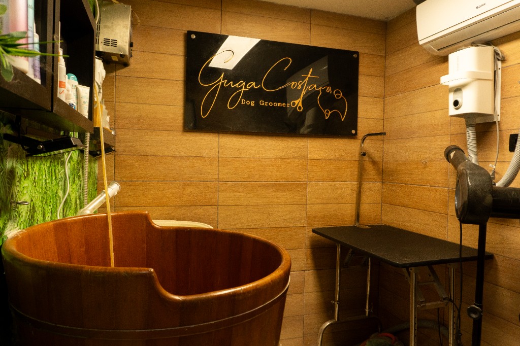 Sala de banho com ofurô de madeira, acabamento em pastilhas claras e torneira à vista.